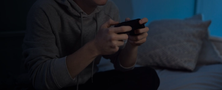Teen boy in a hoodie plays video games on a couch.